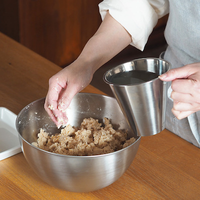 潰した大豆に塩切り麹を混ぜていきます。手で潰しながらよく混ぜ合わせてください。ある程度混ざったら取っておいた煮汁(種水)を少しずつ足して硬さを調整します。